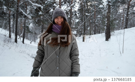 A beautiful young woman in winter clothes is happily spending her free time in a snowy forest. She enjoys the first snow. Active winter recreation. 137668185