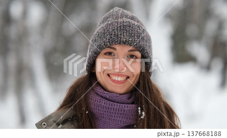 A beautiful young woman in winter clothes is happily spending her free time in a snowy forest. She enjoys the first snow. Active winter recreation. 137668188
