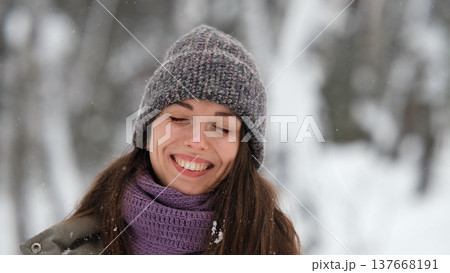 A beautiful young woman in winter clothes is happily spending her free time in a snowy forest. She enjoys the first snow. Active winter recreation. 137668191
