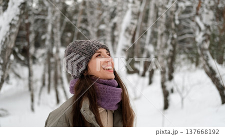 A beautiful young woman in winter clothes is happily spending her free time in a snowy forest. She enjoys the first snow. Active winter recreation. 137668192