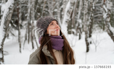 A beautiful young woman in winter clothes is happily spending her free time in a snowy forest. She enjoys the first snow. Active winter recreation. 137668193