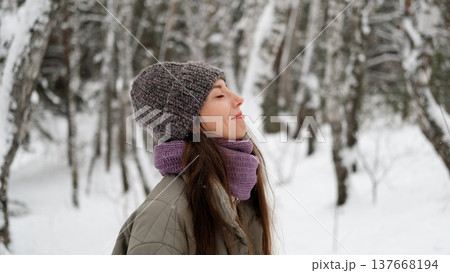 A beautiful young woman in winter clothes is happily spending her free time in a snowy forest. She enjoys the first snow. Active winter recreation. 137668194