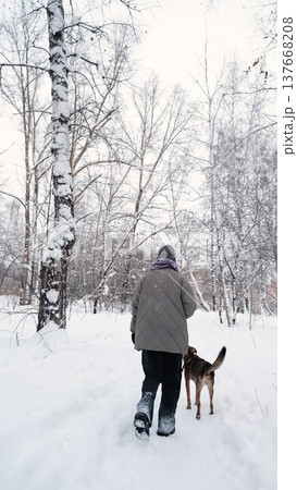 A young woman relaxes during a walk in a winter forest with her dog. A young woman relaxes during a walk in a winter forest with her dog. 137668208