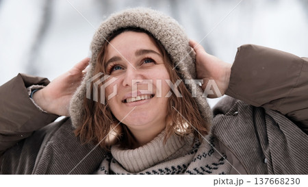 A beautiful woman in winter clothing enjoys her free time in a snowy forest. Portrait of a woman enjoying the first snow. Active winter recreation. 137668230