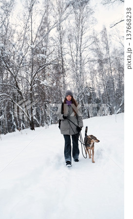 A young woman relaxes during a walk in a winter forest with her dog. A young woman relaxes during a walk in a winter forest with her dog. 137668238