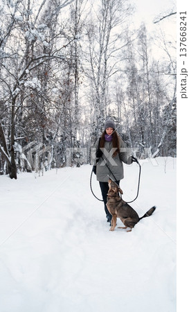 A young woman relaxes during a walk in a winter forest with her dog. 137668241