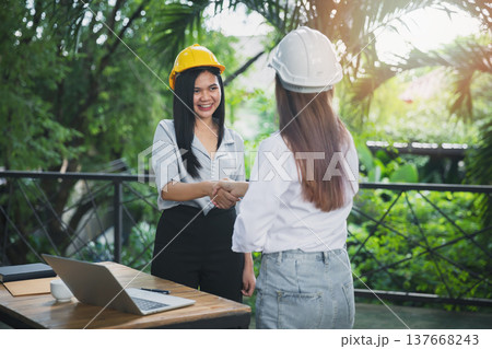 Two asian female architect and engineer in protective helmets shaking hands after meeting. Success collaboration concept. 137668243