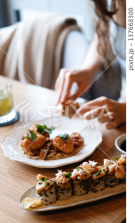 A beautiful girl eats Japanese sushi rolls with chopsticks, smiling with pleasure A beautiful girl eats Japanese sushi rolls with chopsticks, smiling with pleasure 137668300
