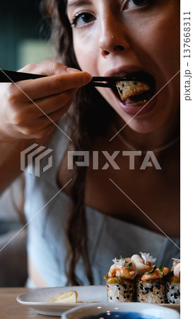 A beautiful girl eats Japanese sushi rolls with chopsticks, smiling with pleasure 137668311