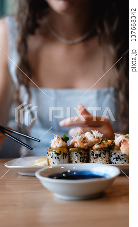 A beautiful girl eats Japanese sushi rolls with chopsticks, smiling with pleasure A beautiful girl eats Japanese sushi rolls with chopsticks, smiling with pleasure 137668342