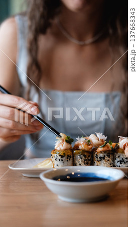 A beautiful girl eats Japanese sushi rolls with chopsticks, smiling with pleasure A beautiful girl eats Japanese sushi rolls with chopsticks, smiling with pleasure 137668343