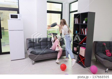 Friends enjoying a playful afternoon in a cozy living room filled with colorful balloons and laughter in a sunlit apartment Friends enjoying a playful afternoon in a cozy living room filled with colorful balloons and laughter in a sunlit apartment 137668505