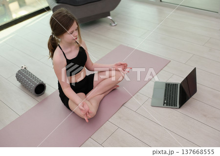 Young girl practices yoga in a serene indoor space while following an online class on her laptop during a bright afternoon 137668555