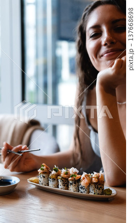 A beautiful girl eats Japanese sushi rolls with chopsticks, smiling with pleasure 137668698