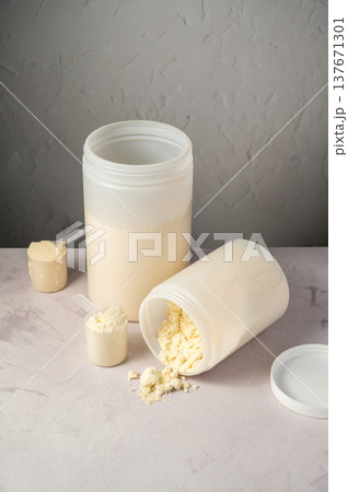 Protein powder in scoops with white plastic protein tubes, jars in background. Body building, muscle growth and food supplement concept Protein powder in scoops with white plastic protein tubes, jars in background. Body building, muscle growth and food supplement concept 137671301