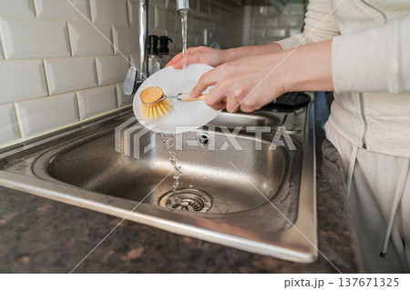 Washing dishes. Eco-friendly kitchen wooden brush. Woman washing a plate with bamboo brush. Waste-free, eco-friendly concept 137671325