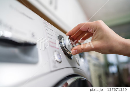 Smart home appliances. Adjusting washing machine setting. Hand turning the dial of a modern washing machine. Daily chores 137671329