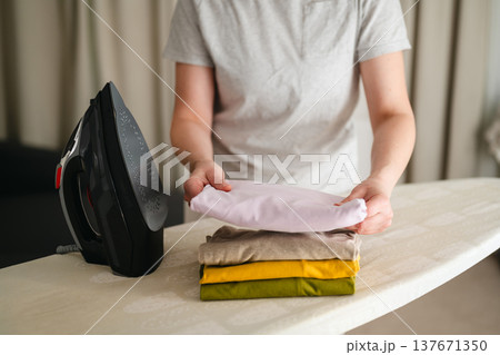 Ironing clothes. Woman ironing t-shirts at home. Daily chores. Laundry day. Gender roles. Ironing clothes. Woman ironing t-shirts at home. Daily chores. Laundry day. Gender roles. 137671350