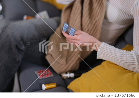 Holding medication on a cozy couch while wrapped in a blanket, reflecting on health and self-care in a comfortable space Holding medication on a cozy couch while wrapped in a blanket, reflecting on health and self-care in a comfortable space 137671666