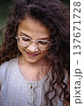 Close up portrait of a smiling young girl with long curly hair and glasses looking down 137671728