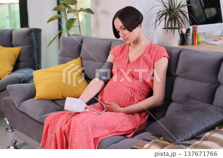 Expecting mother monitors health at home in cozy living room filled with soft cushions and natural light Expecting mother monitors health at home in cozy living room filled with soft cushions and natural light 137671766