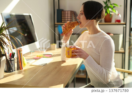 Enjoying a warm croissant and coffee at a cozy home office during a bright morning Enjoying a warm croissant and coffee at a cozy home office during a bright morning 137671780