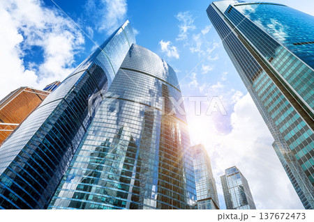 Low angle view of modern glass skyscrapers in Moscow City business district against blue sky with clouds. Contemporary financial architecture in Russia. Low angle view of modern glass skyscrapers in Moscow City business district against blue sky with clouds. Contemporary financial architecture in Russia. 137672473