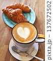 Cup of latte with heart-shaped foam art served with fresh croissant on a rustic wooden table. 137672502