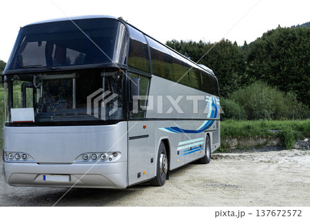 Grey tourist coach bus standing in three quarter view on a parking lot surrounded by green trees. Travel and tourism transport concept 137672572