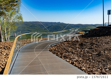 Curved Metal Walkway Observation Deck With Glass Railing Overlooking Mountains And Lake Viewpoint Curved Metal Walkway Observation Deck With Glass Railing Overlooking Mountains And Lake Viewpoint 137672811