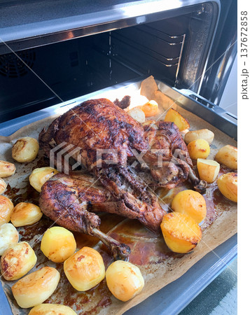 A whole chicken is placed in the oven with potatoes. The dish is being cooked for dinner. The kitchen is warm and smells delicious as the food bakes 137672858
