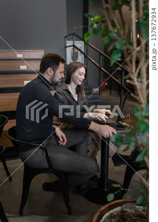 Team collaborating and pointing at computer in green-themed office environment with large decorative tree. Office collaboration, computer work, greenery, teamwork, workspace. Team collaborating and pointing at computer in green-themed office environment with large decorative tree. Office collaboration, computer work, greenery, teamwork, workspace. 137672934