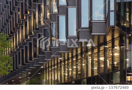 Defined by the sharp convergence of steel and glass, the structure contemporary facade unfolds like a luminous accordion, capturing a shifting dance of light and shadow. 137672980