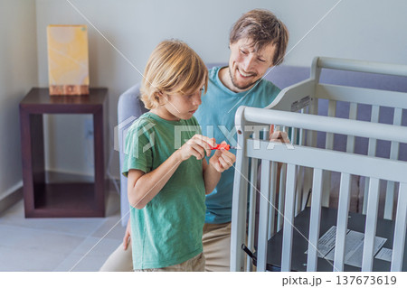 Father and older brother assembling a baby crib at home, preparing for a newborn arrival. Warm family moment full of care and anticipation. Parenthood, sibling bond and home preparation concept Father and older brother assembling a baby crib at home, preparing for a newborn arrival. Warm family moment full of care and anticipation. Parenthood, sibling bond and home preparation concept 137673619