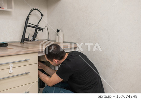 A plumber is replacing a faucet in the kitchen. 137674249