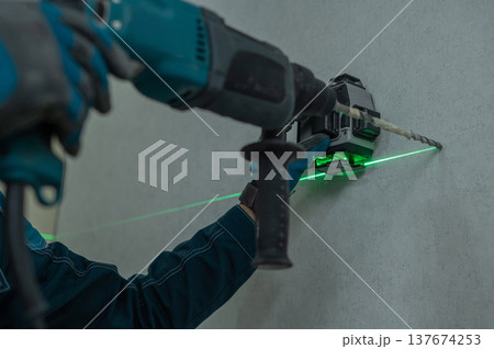 A man measures distances with a laser level and drills into a wall with a hammer drill. 137674253