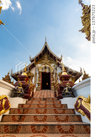 Exterior of Wat Rajamontean in Chiang Mai at sunset with golden temple entrance, naga stair guardians and dramatic sky. Historic Lanna style site offering cultural travel appeal. 137675223