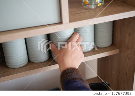 Hand reaches for ceramic dishes on a wooden shelf 137677392