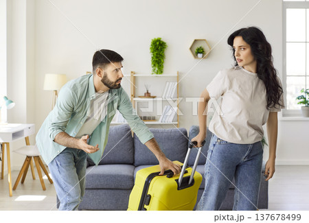 Angry couple arguing at home as partner leaves with bright yellow suitcase 137678499
