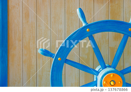 Close-up of blue wooden ship steering wheel mounted on a light wooden wall background. Nautical themed decoration with copy space, symbol of navigation, leadership, travel and maritime adventure 137678866