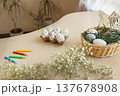 White eggs with simple designs for coloring in a tray and other Easter decor, markers on a table at home against a background of houseplants, DIY Easter preparations 137678908