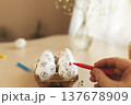 Close-up of person decorating Easter eggs with red marker. White eggs with hand-drawn hearts and flowers placed in an egg carton on table. Creative Easter preparation, DIY holiday decoration 137678909