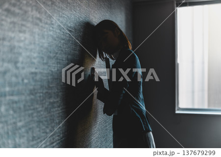 壁に寄りかかり悩む女性のシルエット （シネマティックフォト） 137679299