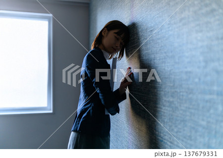 スーツ姿の女性が壁に寄りかかり悩んでいる （シネマティックフォト） 137679331