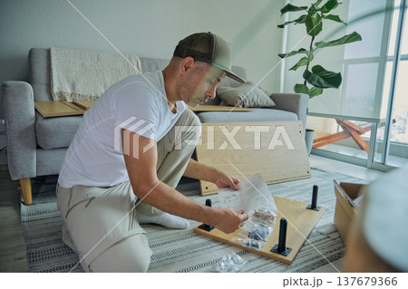 Man assembling flat pack furniture in living room Man assembling flat pack furniture in living room 137679366