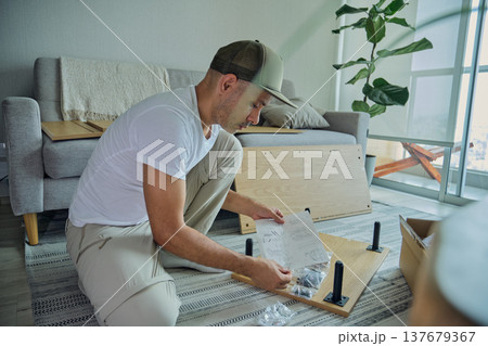 Man assembling furniture reading instruction manual at home 137679367