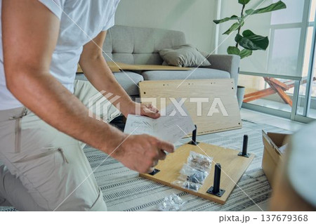 Man assembling furniture piece following instructions at home 137679368