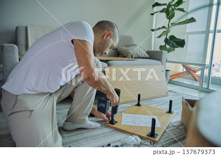 Man assembling furniture with power drill in living room 137679373