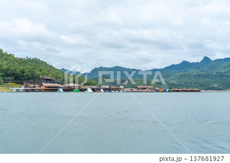 Floating resort and inflatable water park on a calm lake with lush green mountains under a cloudy sky. Scenic summer destination for family vacations and outdoor leisure activities. Floating resort and inflatable water park on a calm lake with lush green mountains under a cloudy sky. Scenic summer destination for family vacations and outdoor leisure activities. 137681927