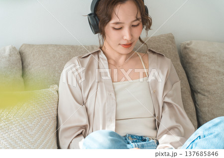 家でソファーに座ってヘッドホンで音楽を聴くリラックスした女性 家でソファーに座ってヘッドホンで音楽を聴くリラックスした女性 137685846